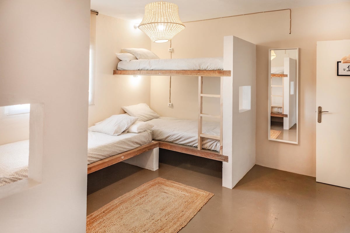 A compact bedroom with a bunk bed, a small desk, and a mirror on the wall.