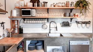 A kitchen with a microwave, sink, and dish rack. There are shelves with jars and glasses, and a potted plant. - Wild House Tarifa - Hostel (Tarifa)