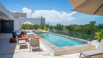 Uma área de piscina no terraço com espreguiçadeiras, uma piscina pequena e vista para o horizonte da cidade.