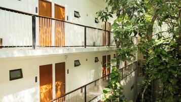Un immeuble à plusieurs étages, doté de balcons, de portes en bois et offrant une vue sur la verdure.