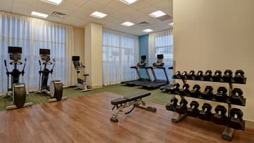 A gym with treadmills, elliptical machines, a bench press, and a rack of dumbbells.