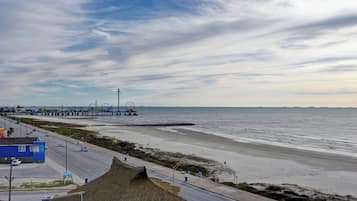 Una carretera costera con playa, muelle y una construcción de techo de paja.