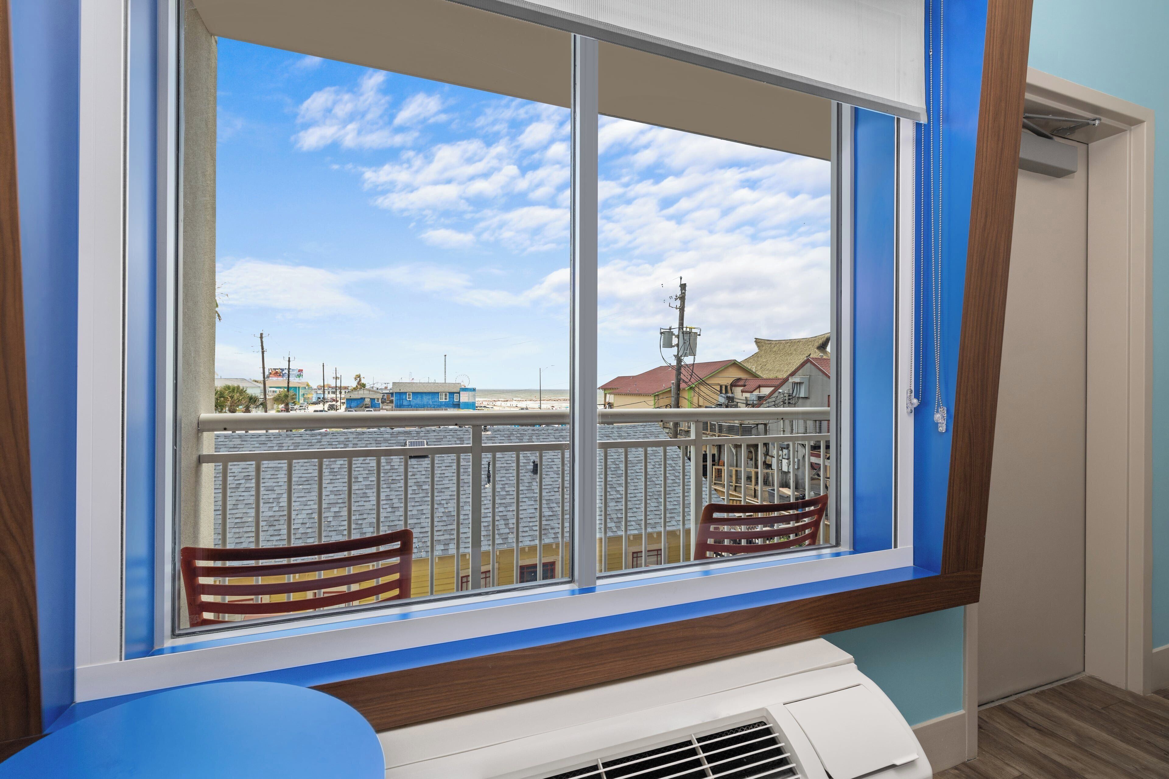 A room with a large window, a white air conditioning unit, and a view of a building with a balcony.