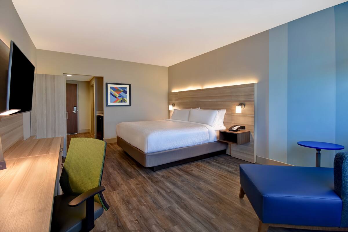 A hotel room with a bed, a desk, a chair, a small table, and a TV.