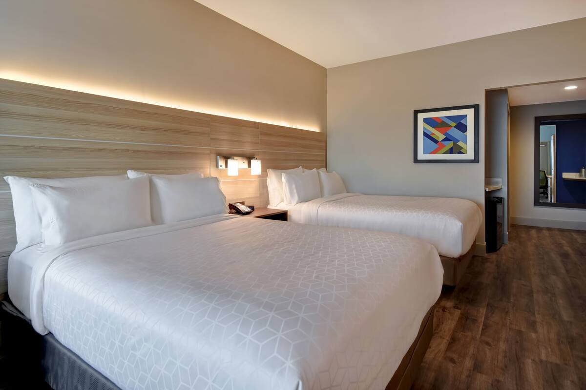 A hotel room with two beds, a wooden headboard, a wall-mounted light, and a framed abstract painting.