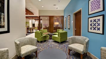 Een hotel lobby met groene beklede stoelen, een ronde tafel en een kamerbreed tapijt met dessin.