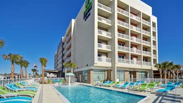 A hotel with a pool area, multiple balconies, and palm trees.