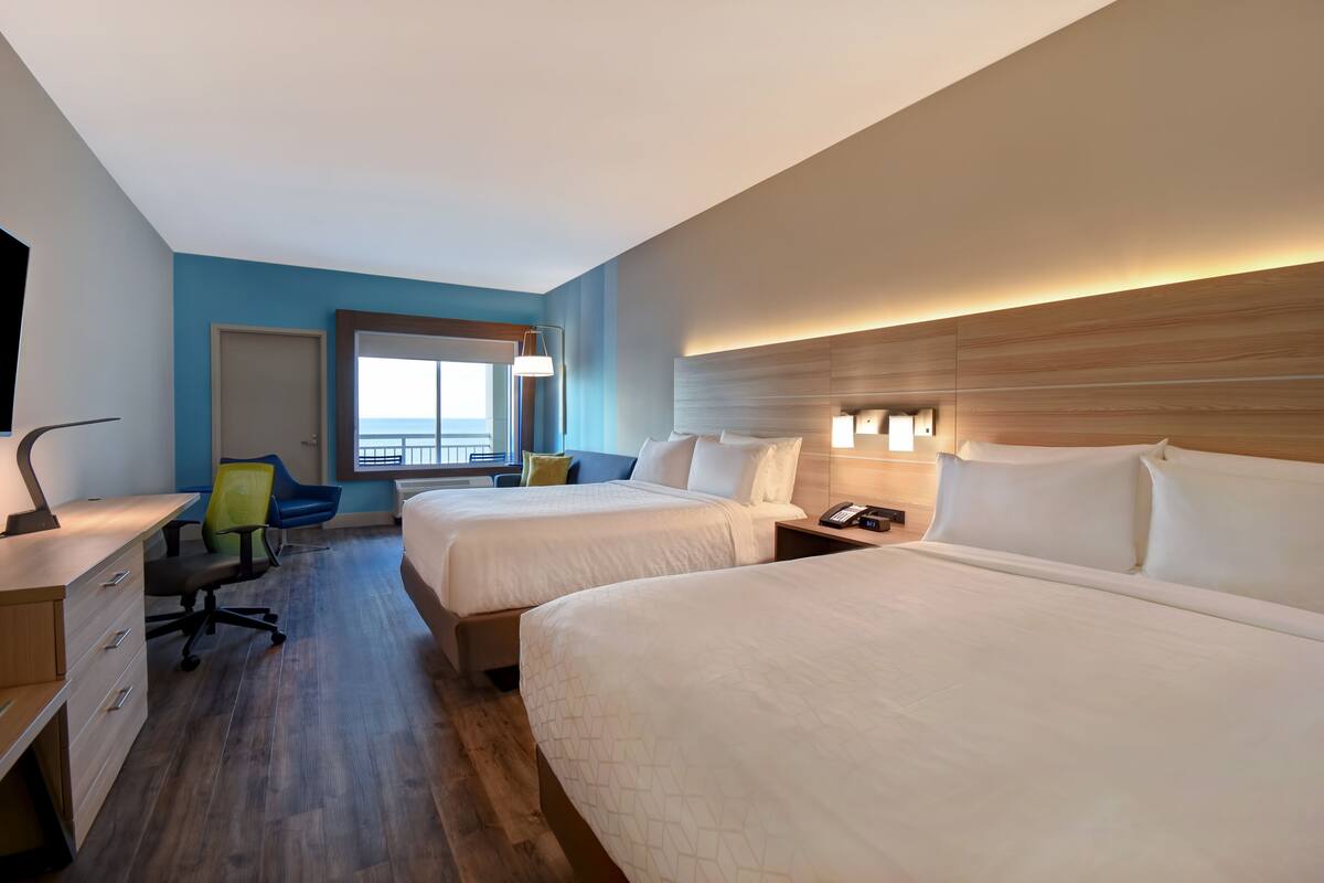 A hotel room with two beds, a desk, a chair, and a window with a view.