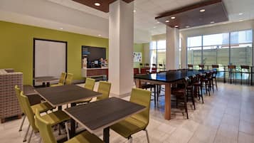 A modern dining area with green walls, a coffee station, and large windows.