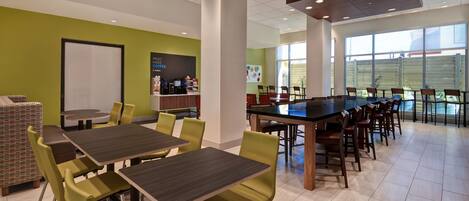 A modern dining area with green walls, a coffee station, and large windows.