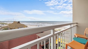 A balcony with a view of the beach and ocean, a thatched-roof structure, and a fenced area with yellow umbrellas. - Holiday Inn Express & Suites Galveston Beach by IHG (Galveston)