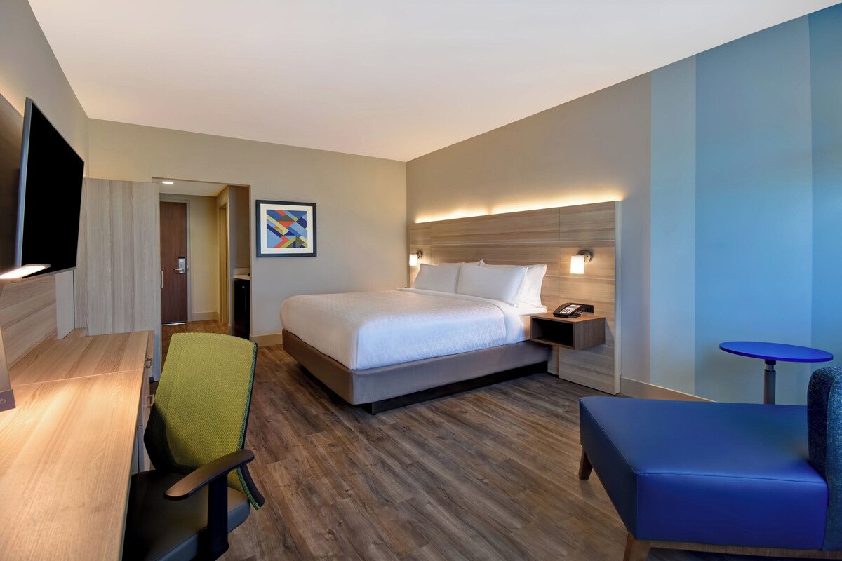 A hotel room with a bed, a desk, a chair, a small table, and a TV.