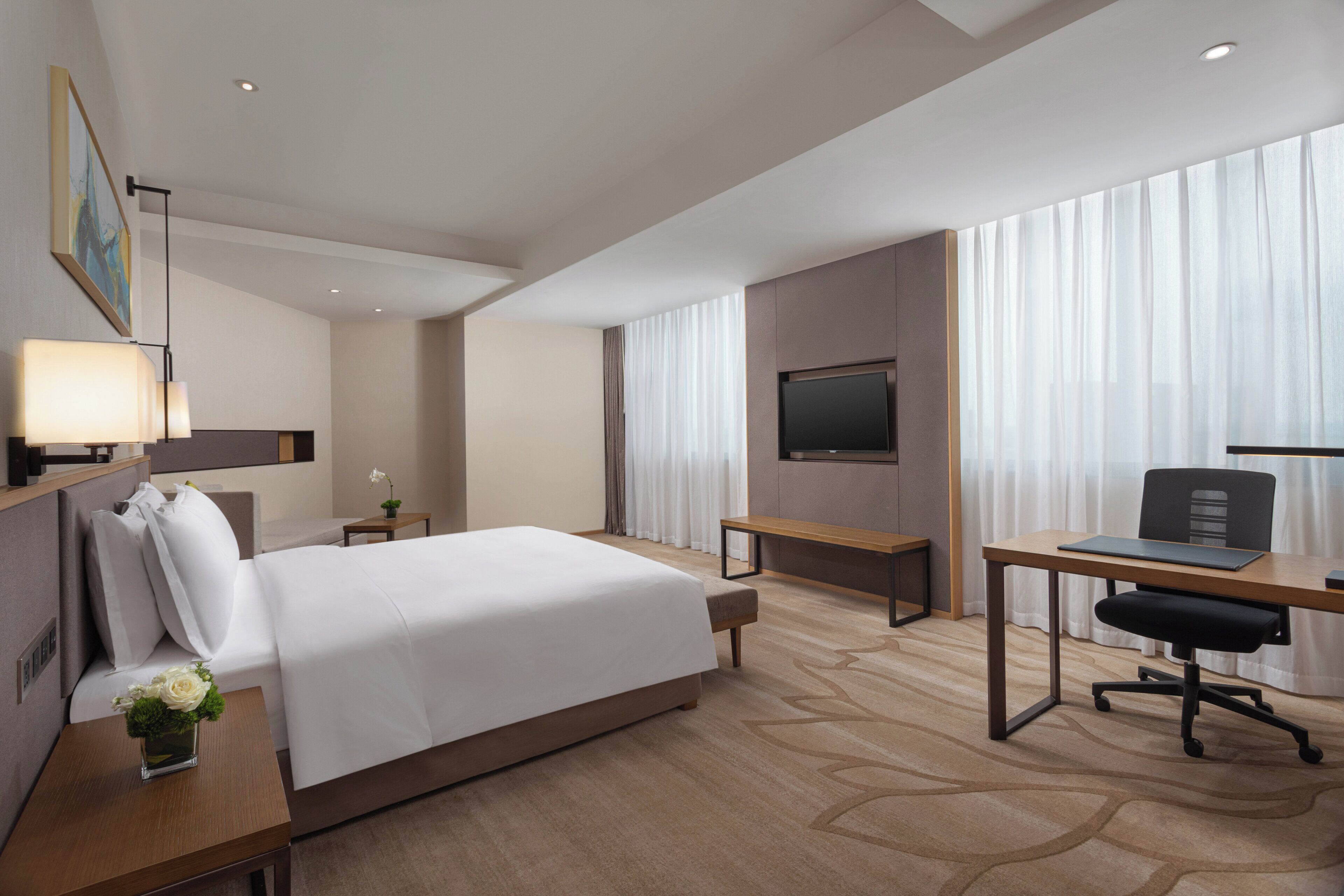 Ein Hotelzimmer mit Bett, Schreibtisch, Stuhl, Fernseher und einem Fenster mit Vorhängen.