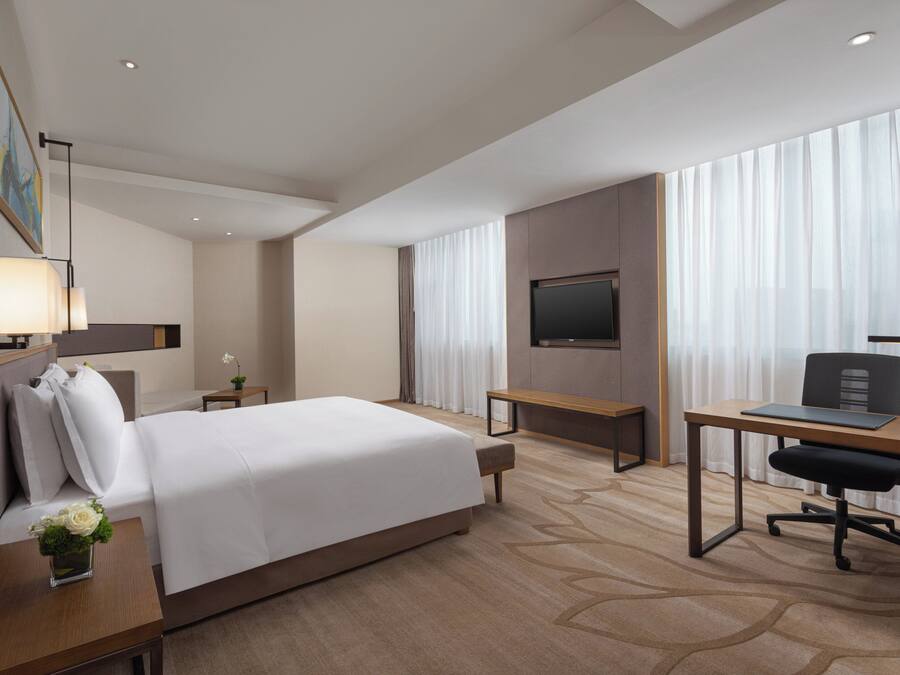 Ein Hotelzimmer mit Bett, Schreibtisch, Stuhl, Fernseher und einem Fenster mit Vorhängen.
