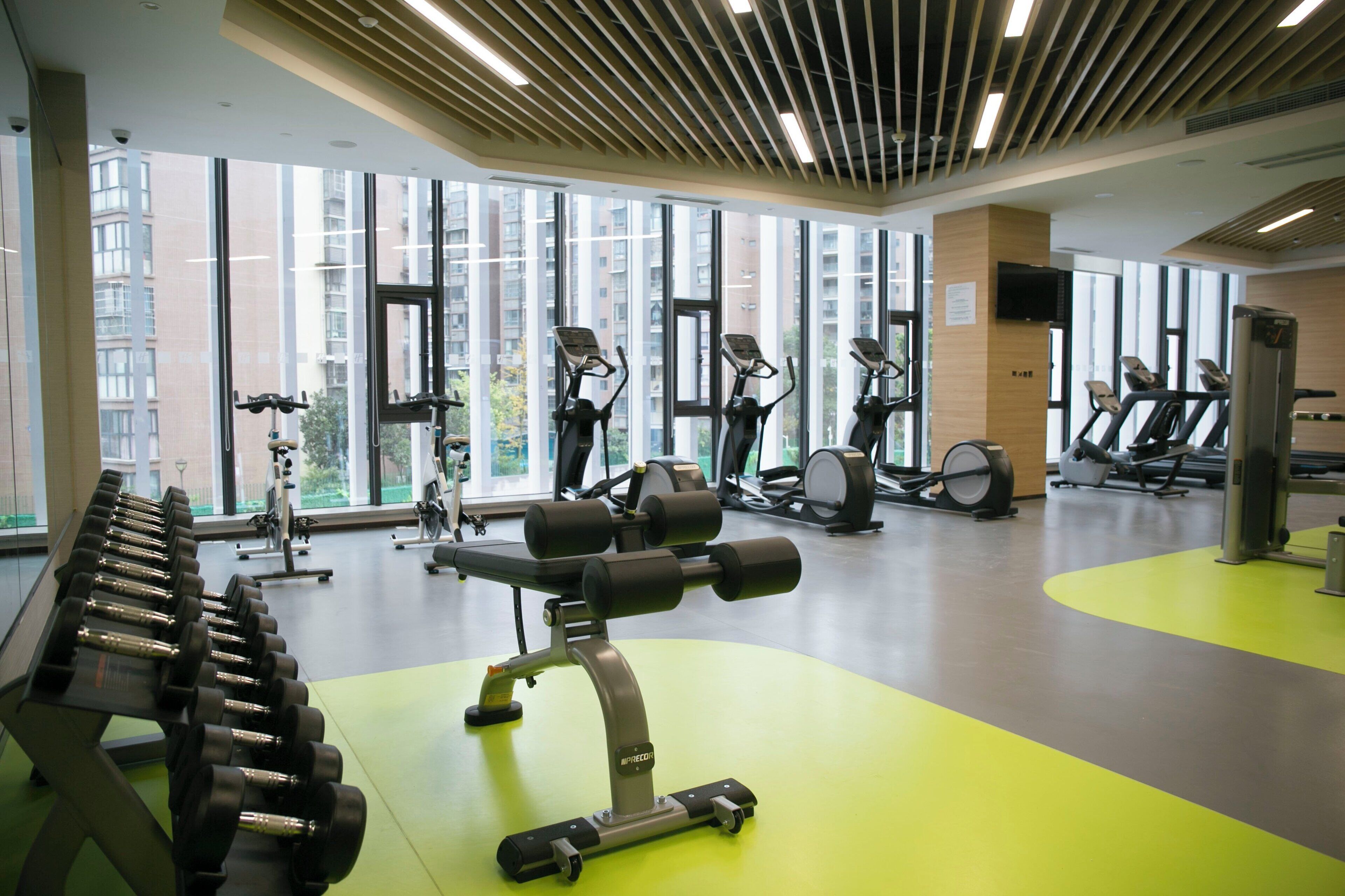 A gym with exercise equipment, large windows, and a green floor.