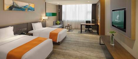 A hotel room with two beds, a desk, a TV, and a large window with curtains.