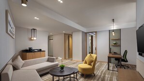 Une chambre d’hôtel moderne équipée d’un canapé, d’un fauteuil, d’une table ronde, d’une télévision et d’un coin cuisine.