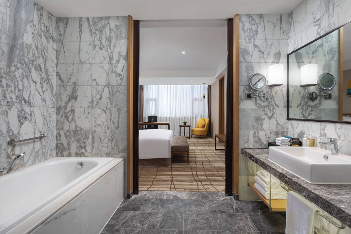 A modern hotel bathroom with a bathtub, a large mirror, and a vanity with a sink.