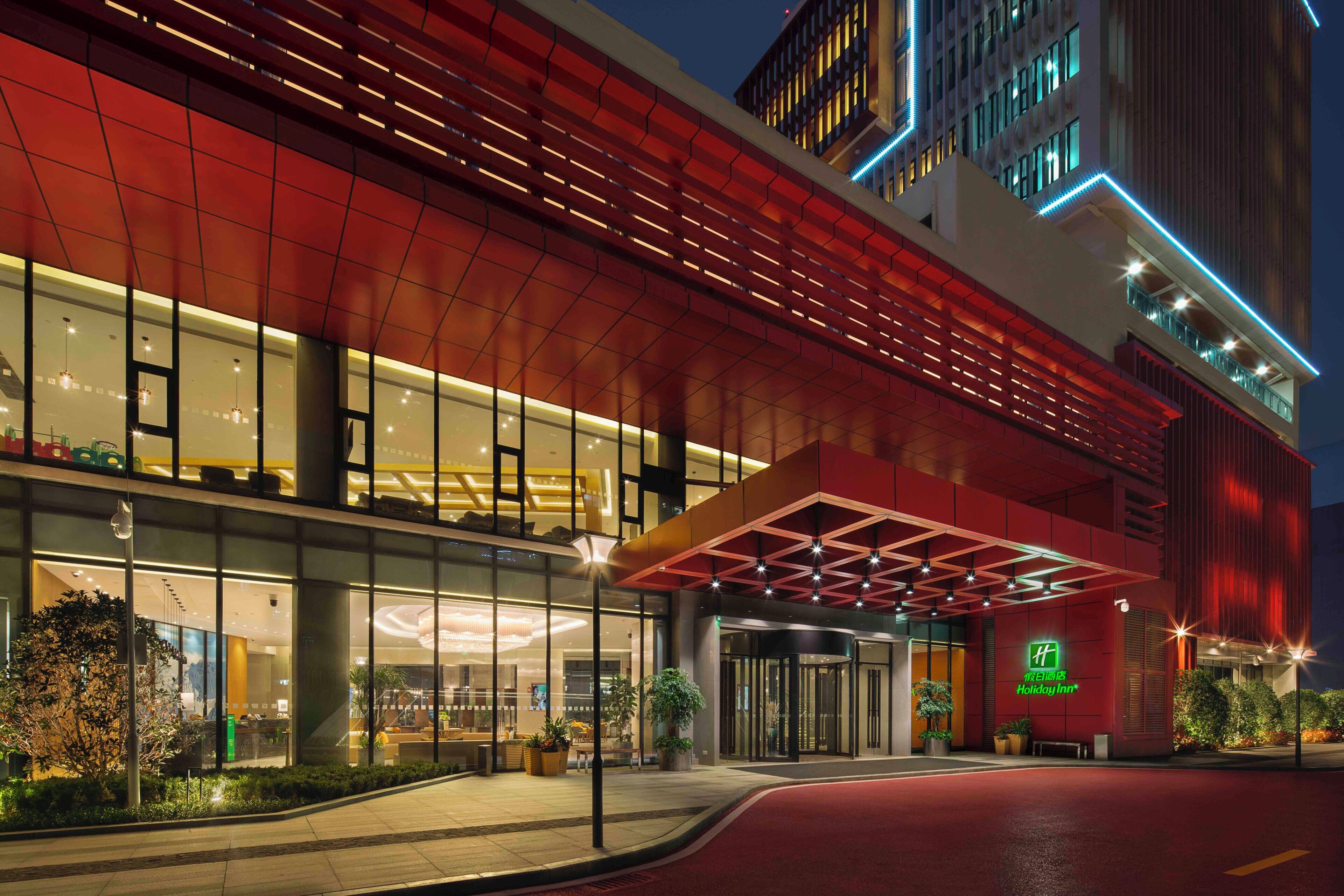 A hotel entrance with a glass facade, a red awning, and a Holiday Inn sign.