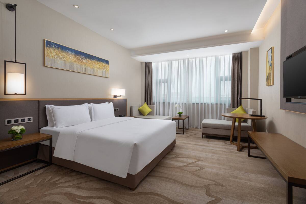 A hotel room with a large bed, a desk, a chair, a TV, and a window with curtains.