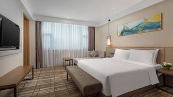 A hotel room with a large bed, a small bedside table, a bench, a TV, and a painting on the wall.