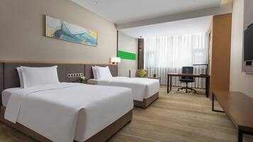 Quarto de hotel com duas camas, uma escrivaninha, uma cadeira, uma televisão e uma janela com cortinas.