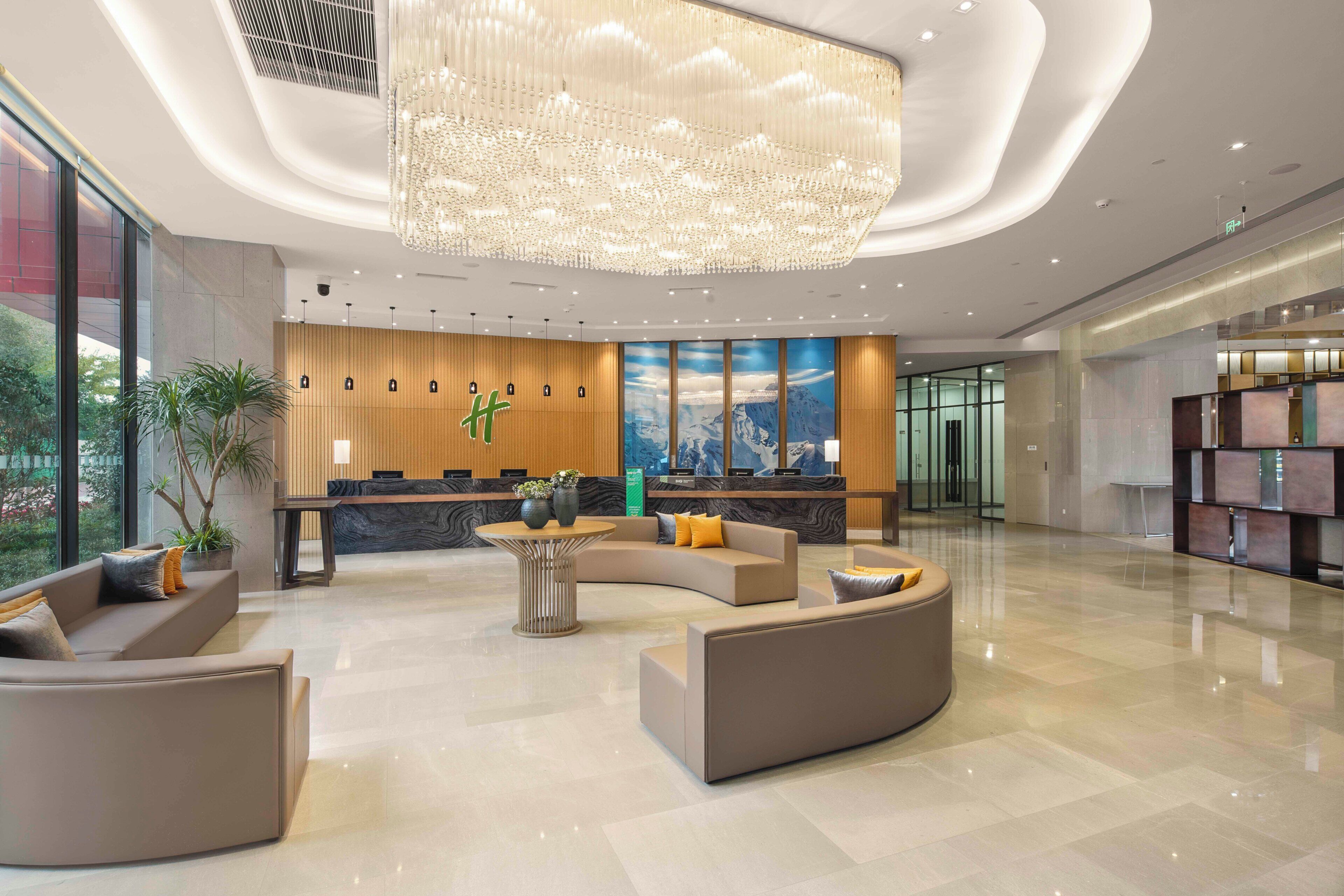 A modern lobby with a reception desk, seating area, and a large chandelier.