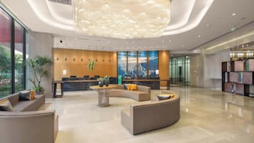 A modern lobby with a reception desk, seating area, and a large chandelier.