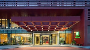 Une entrée d’hôtel moderne avec une façade en verre, un espace d’entrée abrité et une enseigne indiquant qu’il s’agit d’un Holiday Inn.