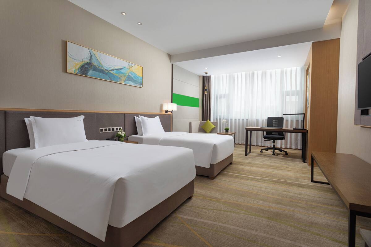 A hotel room with two beds, a desk, a chair, a TV, and a window with curtains.