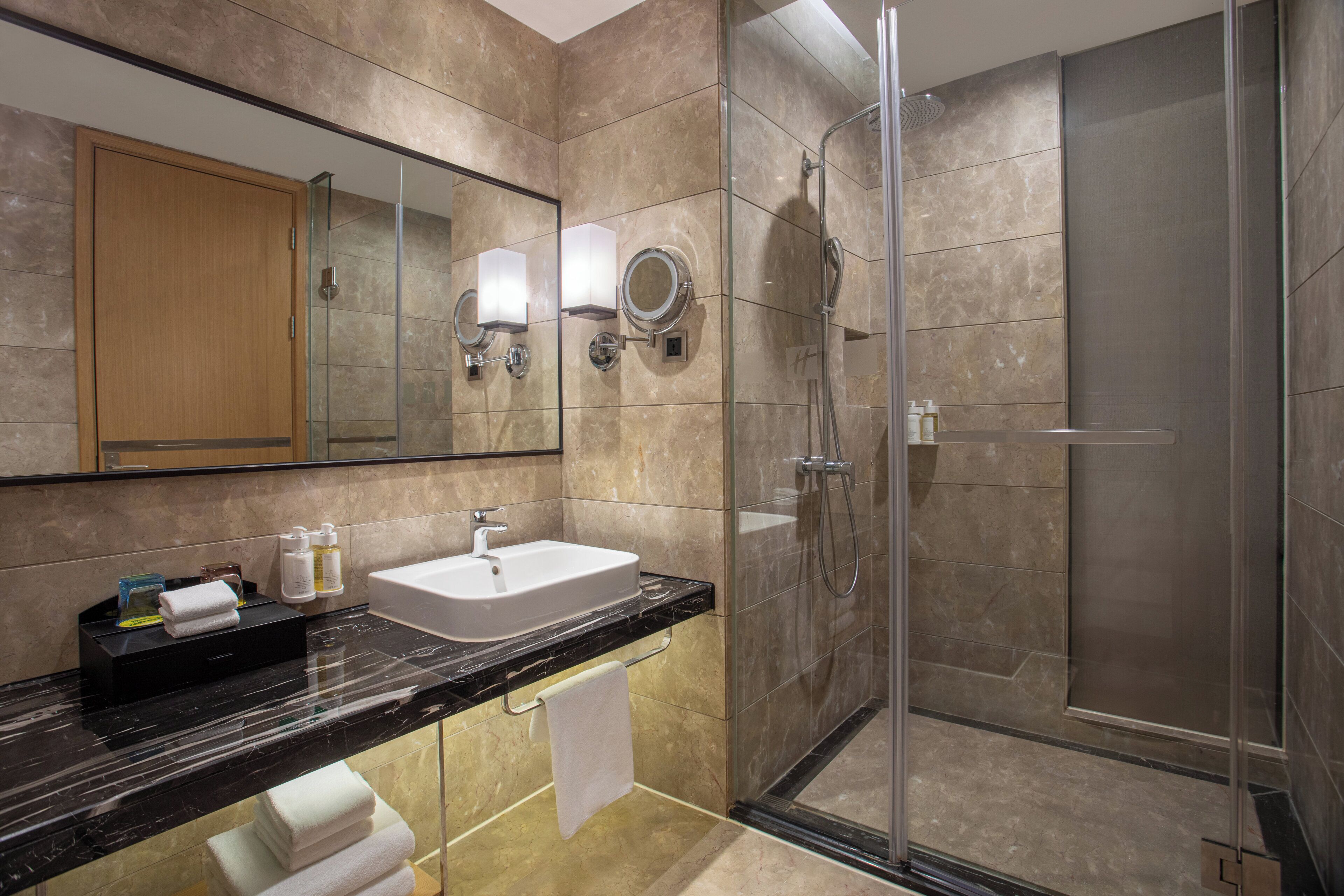 A modern bathroom with a glass-enclosed shower, a marble sink, and a large mirror.