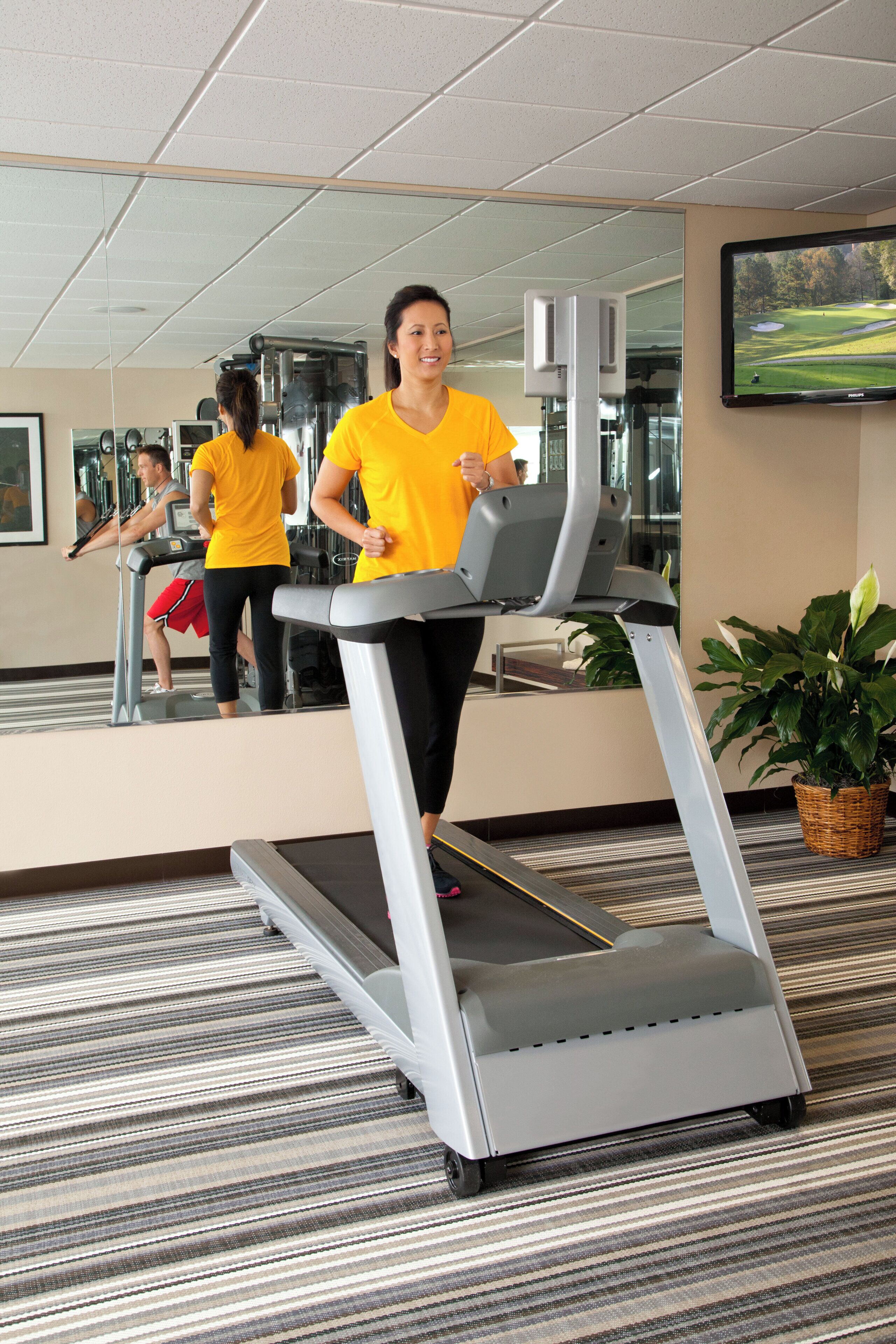 A gym with treadmills, exercise equipment, and a large mirror reflecting the space.