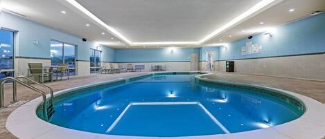 Une piscine intérieure avec un sol carrelé, un escalier d’accès et un espace détente avec des chaises.