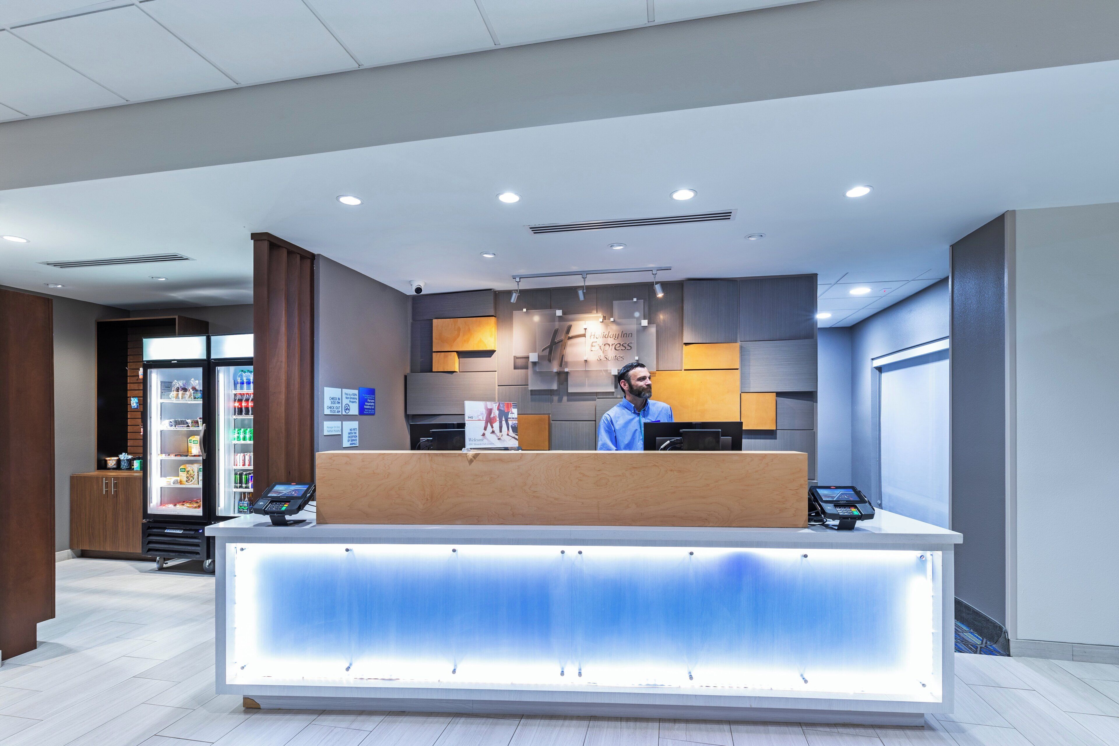 A hotel reception desk with a digital check-in kiosk, a man standing behind it, and a view of the lobby area.