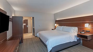 Habitación de hotel con una cama grande, un televisor, un cabecero de madera y una mesita de noche con lámpara.