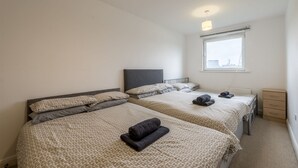 Une chambre d’hôtel avec deux lits, une fenêtre donnant sur la ville, une table de chevet et une petite commode.