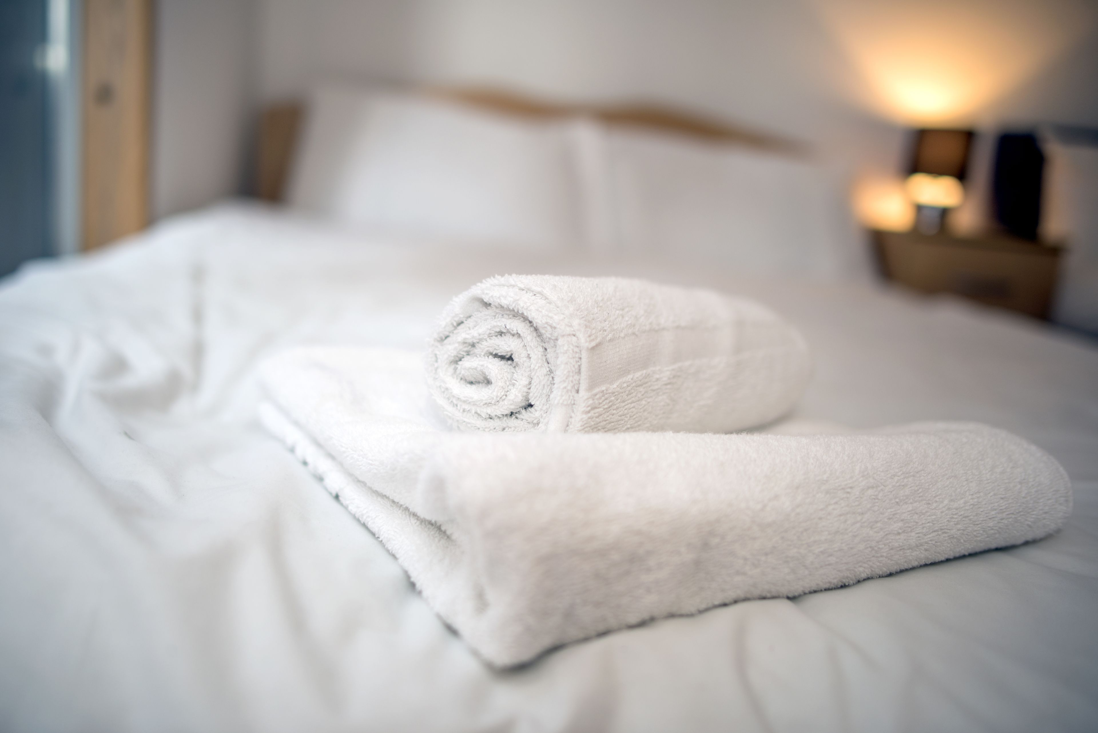 Una cama bien hecha con una toalla blanca enrollada y una lámpara de noche.