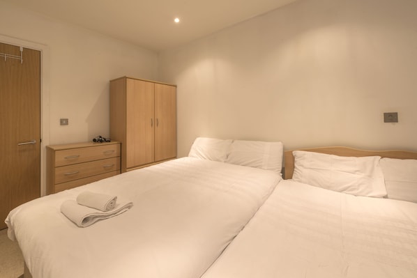 A bedroom with a large bed, a wooden wardrobe, and a bedside table with a lamp.