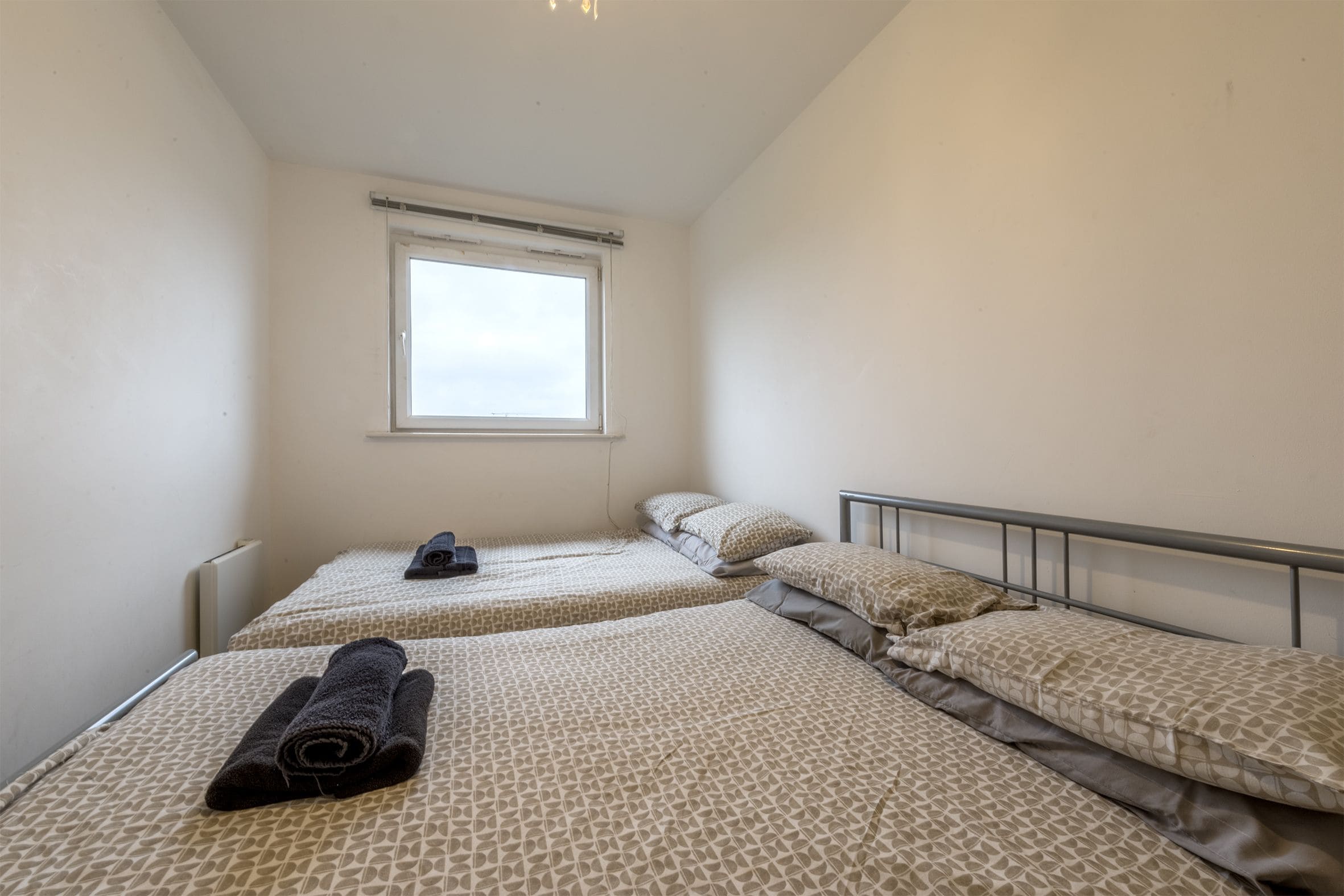 Une petite pièce propre, avec deux lits, une fenêtre et un radiateur.