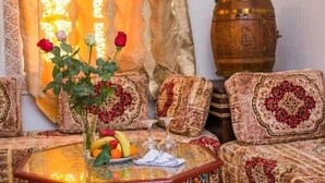 A cozy living area with a sofa set, a glass coffee table with a vase of flowers, and a wooden barrel. - Riad la porte bleue du palais laraichi (Fes)