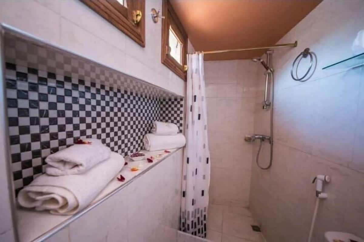 A bathroom with a checkered tile wall, a shower area, and a shelf with folded towels.