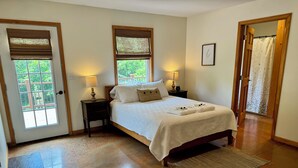 Un dormitorio con una cama, dos mesitas de noche con lámparas, una ventana con persianas, una puerta y una alfombra.