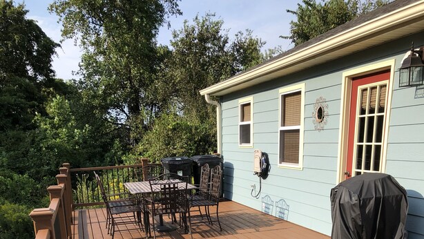 Una terraza con mesa y sillas, una parrilla cubierta y una casa al fondo.
