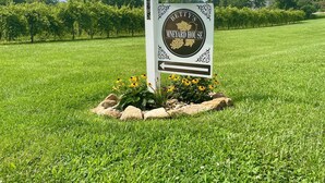 Un letrero indica Betty's Vineyard House en un campo con césped, una valla blanca y un cielo despejado.