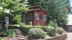 Una casa roja con un letrero que indica que vende huevos, rodeada de un jardín con una escalera de piedra que sube a ella.
