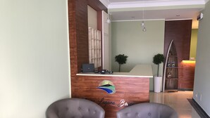 A reception area with a wooden counter, two grey armchairs, and a small desk with a laptop. - Naxos Laguna Beach (Giardini Naxos)