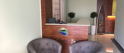 A reception area with a wooden counter, two grey armchairs, and a small desk with a laptop.