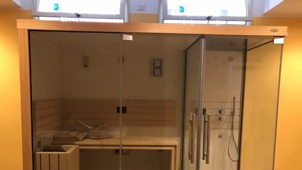 Una sauna con una panchina, porte in vetro e un angolo doccia.