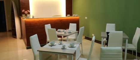 A modern dining area with white chairs and tables, a wooden reception desk, and green walls.