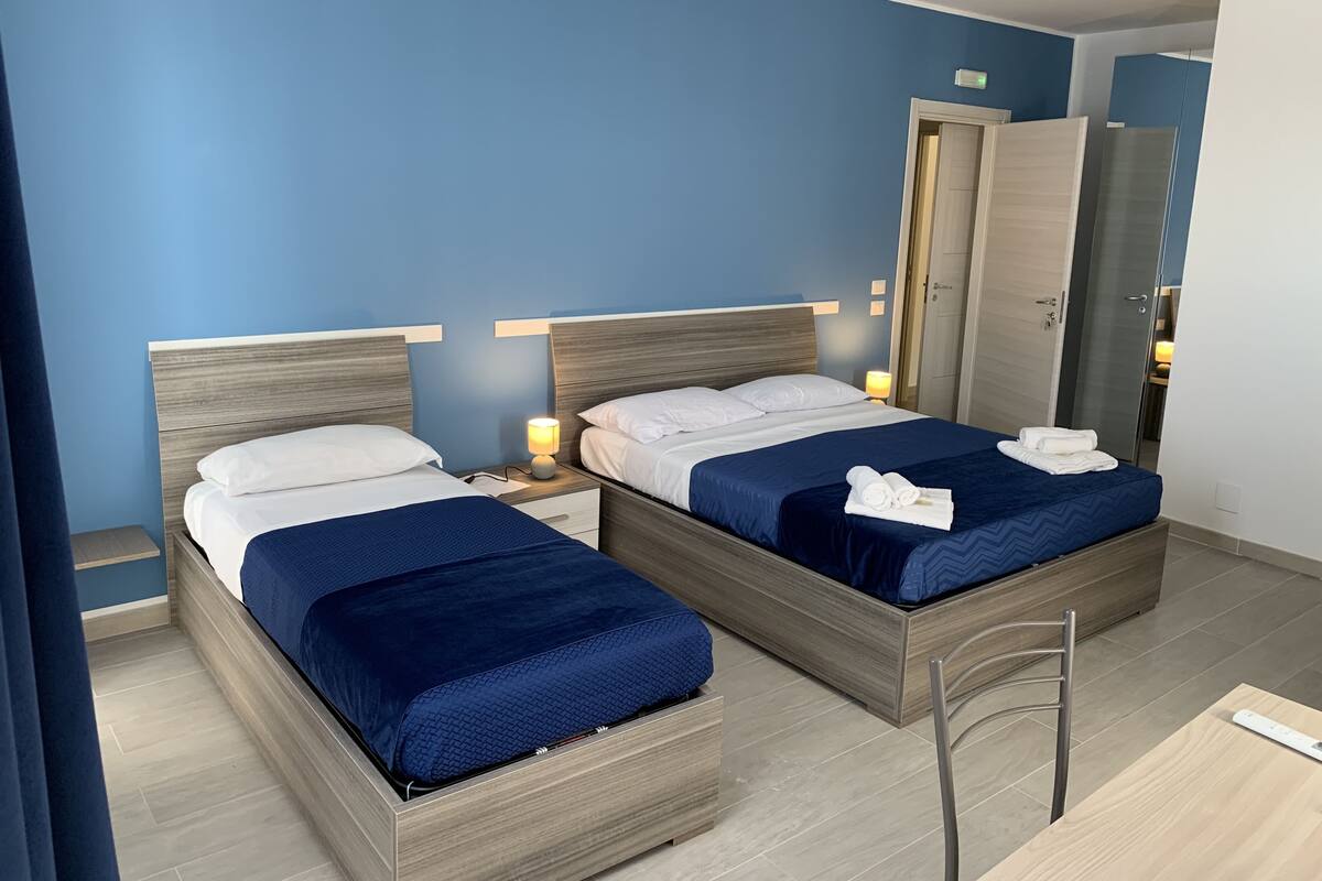 Une chambre d’hôtel avec deux lits, chacun doté d’une tête de lit en bois, d’une table de chevet et d’une lampe. Il y a une porte sur la droite et un miroir au mur.